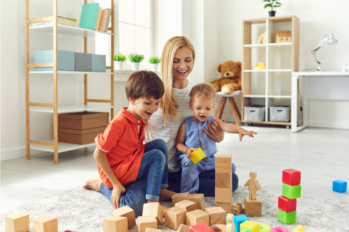 Mom and Children Are Smiling Playing with Toys While Sitting on the Floor in the Living Room. Happy Family